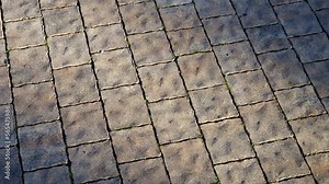 Stone tiles pavement made of granite or marble - pattern of brown floor paving as background. Texture of rough wavy uneven surface revealed by side lighting.