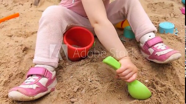 A child scoops sand into a bucket with a scoop