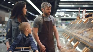 Shop assistant is working in bakery department in supermarket then packing bread roll for nice family mother and son and giving food to attractive woman.