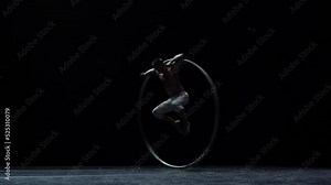Muscular circus artist perform Cyr Wheel on a black background stage in slow motion