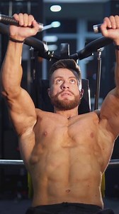 Training muscles. Sportsman pumping his trained body on a simulator. Strong trainer doing workout. Bodybuilder doing exercise on the modern simulator in the gym. Vertical