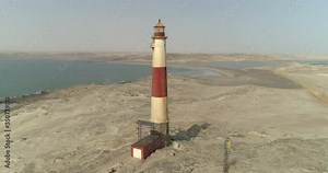 Aerial shot of tall lighthouse at beach near sea against sky, drone panning from left to right over rock formation on sunny day - Luderitz, Namibia Stock Video