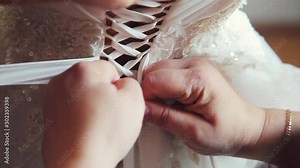 maid of honor helping the bride with her dress. the bride's lace up dress. Bridesmaid tying bow on wedding dress. Woman's hands lace up silk ribbon on bride's corset. Helping to lace up