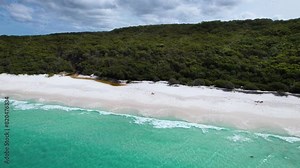 A 4k drone video that flies backwards to reveal more of a beautiful white sand beach with a bright blue ocean as the waves roll calmly against the shore. Hyams Beach, Jervis Bay, New South Wales