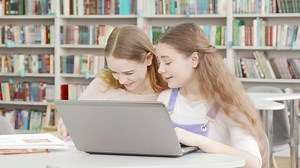 Happy teenage girls laughing while studying together at the library