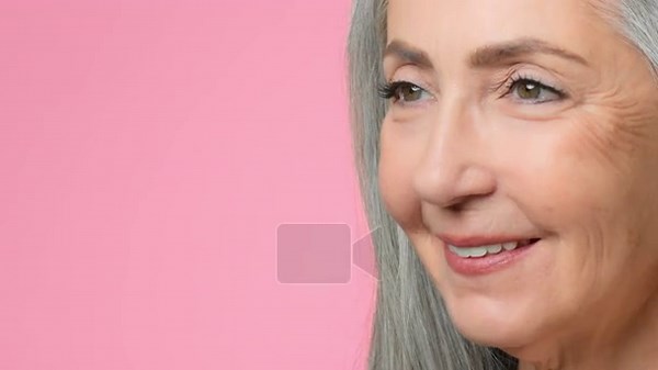 A woman with gray hair smiles while posed against a plain pink background. Her facial expression shows happiness and warmth. This capture highlights her joyful moment Stock Video Footage - Alamy