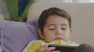 Boy sitting on sofa watching cartoons on the phone.