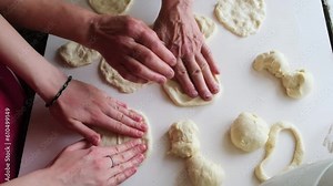 Close-up hands of grandmother and granddaughter while preparing sweet buns. Family cooking raw yeast dough pastry, rustic kitchen table top view.