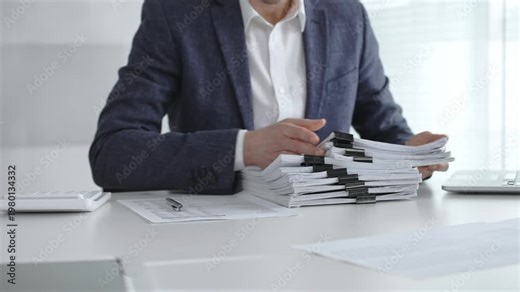 Business professional sorting a large stack of financial reports and tax forms with binder clips on a busy office desk. Audit and taxes