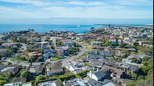 Aerial time lapse in motion over coastal Orange County, California neighborhood and PCH on sunny day with luxury homes below.