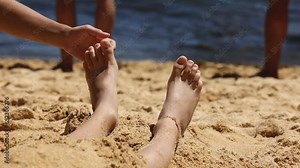 Child, tickling sibling on the beach on the feet with feather, kid cover in sand, smiling, laughing, enjoying some fun