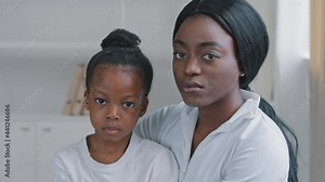 Family portrait sad african american mother caring ethnic woman and upset serious little afro daughter black preschooler child girl sitting hugging looking at camera with worried expression indoors