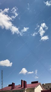 Time lapse of white cumulus clouds on the blue sky over the roofs of residential buildings