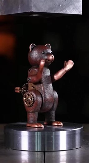 A vintage tin clapping bear toy meets its match under a hydraulic press. Watch as the rhythmic clapping suddenly stops, arms buckle inward, and the adorable mechanical toy collapses in satisfying slow motion with a dramatic bead of oil escaping beneath.