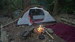 Bushcraft camp site in the wilderness with campfire, axe, and blanket. Fairy lights on a tent in the Blue Ridge Mountains near Asheville, North Carolina.
