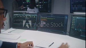 Software programmer sits in front of computer with blockchain network database in monitoring control room. Team of IT technical specialists work with real-time analysis charts on big digital screens.