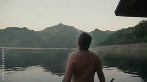 wet man stands by lake. guy is watering himself with bucket. cold water runs down body.happy person after hard physical work. the concept of strength exercises, weight loss, tan, swimming, steam from