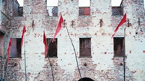 Red flags in front of an ancient castle. Medieval customs and tribal lifestyle. Tall wooden poles with waving red sheets. Heraldic flags, banners, standards and pennons. Clan gathering and authority.