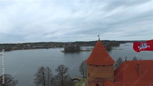 Trakai Island Castle located on an island in a lake. The castle stands tall with its orange rooftops. The area is surrounded by calm waters and trees.