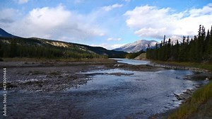 View of the wild Athabasca River with rocky riverbed in a valley near Jasper, Alberta, Canada in the Rocky Mountains with flowing water, coniferous trees and mountains in autumn season.