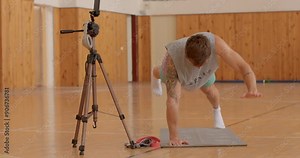 raising arms and legs up man doing one-arm plank exercise indoor gym, recording video, focused stability and strength. Load on the human spine, working out complex strength.