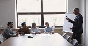 Senior business coach man giving lecture, seminar to diverse professional team, speaking at flipchart, training interns. Mature boss presenting project plan, marketing strategy to employees
