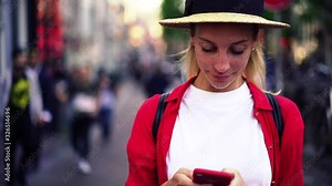 Smiling positive woman in hat feeling happy while read text message on mobile phone, slow motion effect of caucasian female holding cellphone