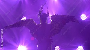 Pretty young actress in the image of the Greek goddess Artemis with golden wings and a headdress poses on stage. Silhouette. Close up.