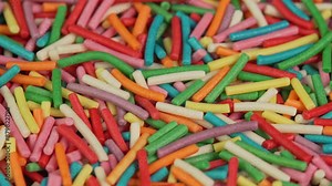 Colored confectionery sprinkles rotate in macro. Culinary topping for desserts and baked goods close up. Colorful rainbow sugar candy sprinkles for donuts