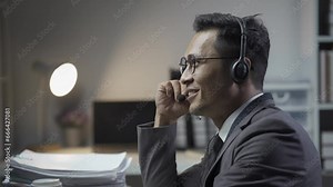 Businessman wearing headset sitting in office using desktop computer talking with customers in video conferencing app. Remote help, virtual meeting by business, negotiation concept