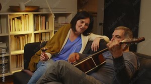 middle age couple relaxing together at home. drinking wine and playing guitar and singing
