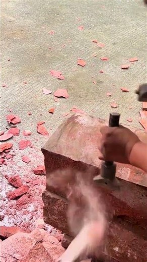 Splitting large red stones manually using a hand held chisel and hammer to shape masonry blocks