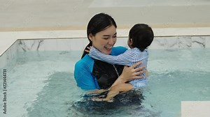 happy mother holding baby in her arms while playing water splashing in a swimming pool