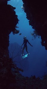 Woman freediver glides in underwater cave with rocks and coral reef in Indonesia