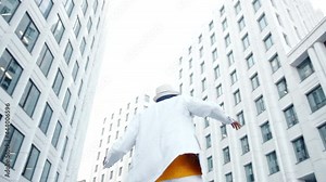 Black man in suit with hat dances on street among buildings