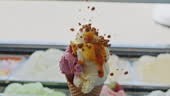 Ice cream Vendor puts brittle on ice cream cone filled with different...