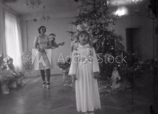 Girl child reciting poem on Christmas tree background in kindergarten New Year celebration, teacher watches. Kid in festive costume in children party. Old film. Archival retro 1960s. Vintage archive