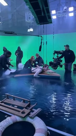 Titanic BTS: How the Sunset Deck Pose Scene Was Filmed 🚢🎥 Step behind the camera and see how this calm sunset deck moment was filmed. The set is built on an elevated platform with a large LED backdrop showing a golden ocean sunset. Bright studio panels hang overhead to sculpt warm light across the actor’s face, matching the sunset glow. The actor stands confidently at the railings, rehearsing posture and expression while crew members in black clothing stand around adjusting cables, camera focu