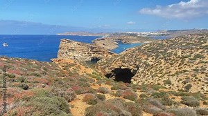 Beautiful Comino Island cliffs with seagulls flying around and boats sailing towards the island. Hiking path over the rugged terrain. High quality 4k footage