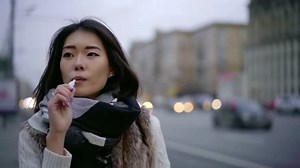 japanese woman is inhaling smoke of vape walking near road in city in autumn day, close-up