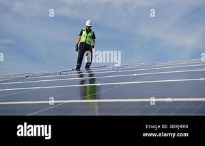 Technician installing solar panels on factory roof for green energy. A skilled technician in safety gear is working on a solar panel installation on rooftop. clean energy renewable power technology.