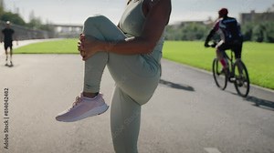 Young African American fitness woman in sportswear stretching body and warming up before jogging in sports hall in morning. Healthy female athlete enjoys training outdoor. Lifestyle exercising in city
