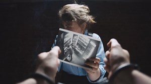 Lady interrogator with cigarette demonstrating photo evidence to suspect. Female detective smoking and interrogating arrested man in handcuffs at police department