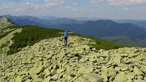 Happy man hiker stands on the top of the mountain with outstretched arms. Male tourist hike up the mountain. Aerial all-round view