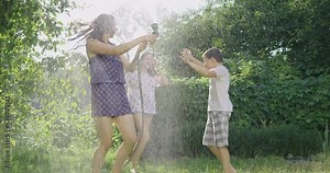 Mother and children play with water from a garden hose. A happy family rests, rejoices and splashes with water in hot summer weather. Watering in the garden near the house.