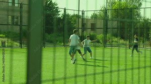 Group of boys playing football on sport playground in sunny day . Many kids play soccer in stadium with green grass and gate . Training , competition , healthy activity for children . Slow motion