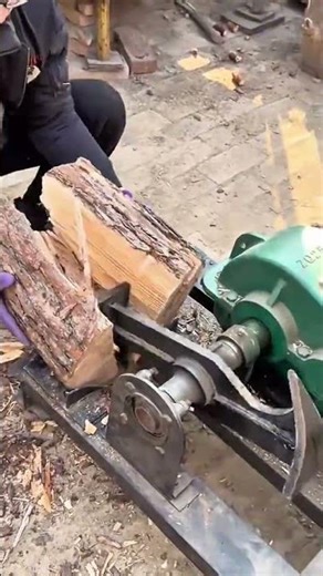 splitting the large brown tree log into smaller pieces using a metal machine tool