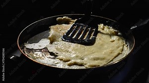 The first pancake is a failure. Unsuccessfully fried pancake is flipped on the pan on a dark background.