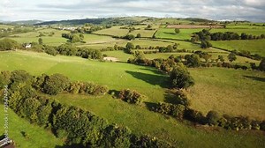 Aerial rolling rural farm hills fields Wales pull. Beautiful green, rock fences, hedgerow and forest tree meadows and rural farms. Rolling hills and gentle valley. Nature and history mingle in harmon