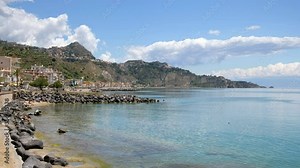 Sicilian beach in Giardini Naxos and ancient Taormina town on a hill in Sicily